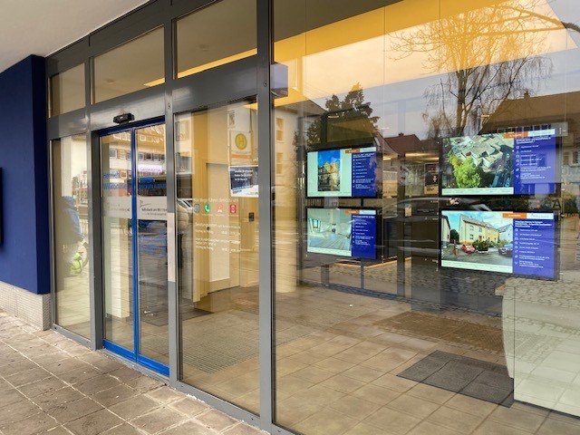Digital property screens beside a glass entrance